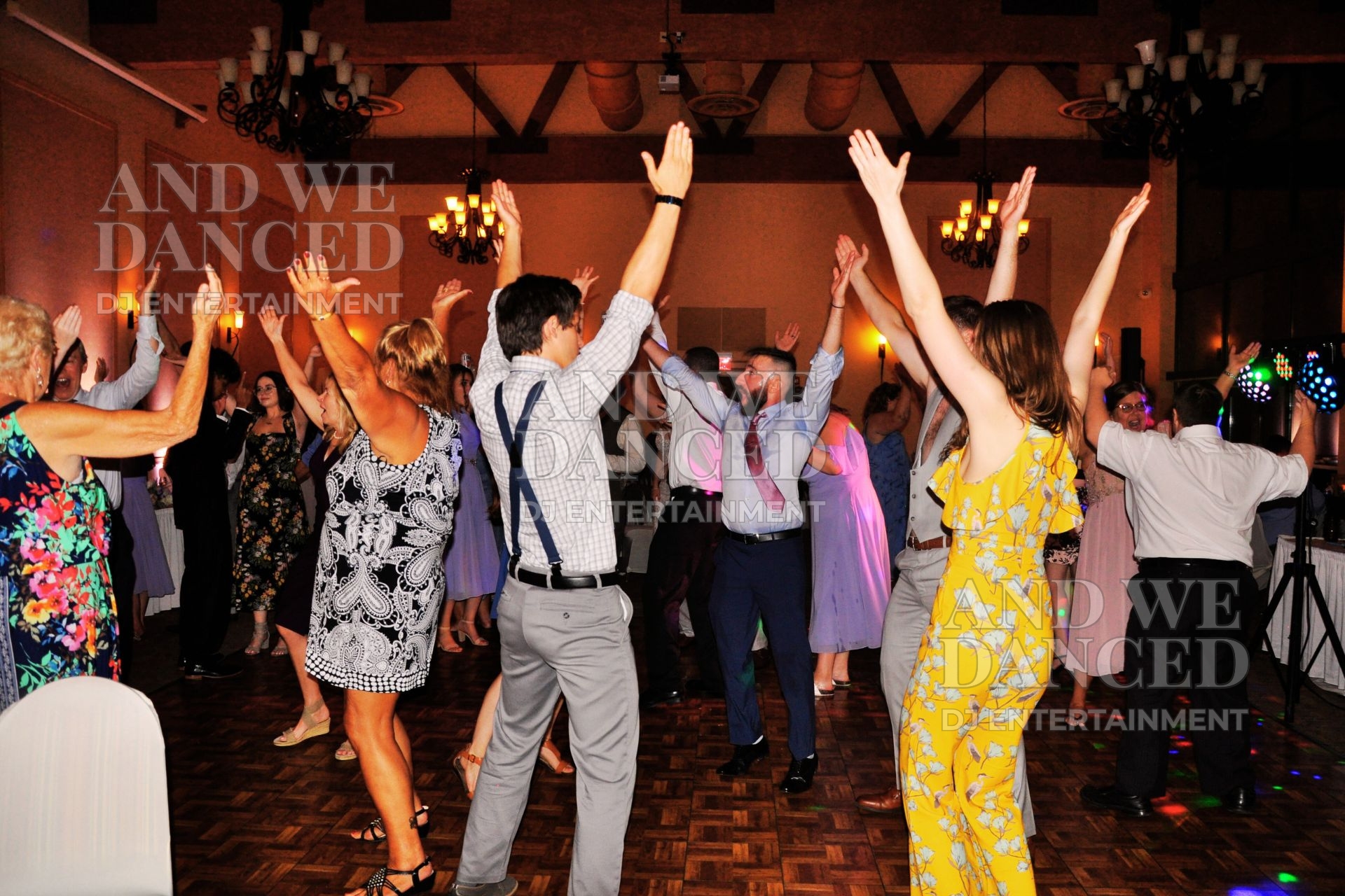 Wedding guests dancing with raised hands on a packed reception dance floor.