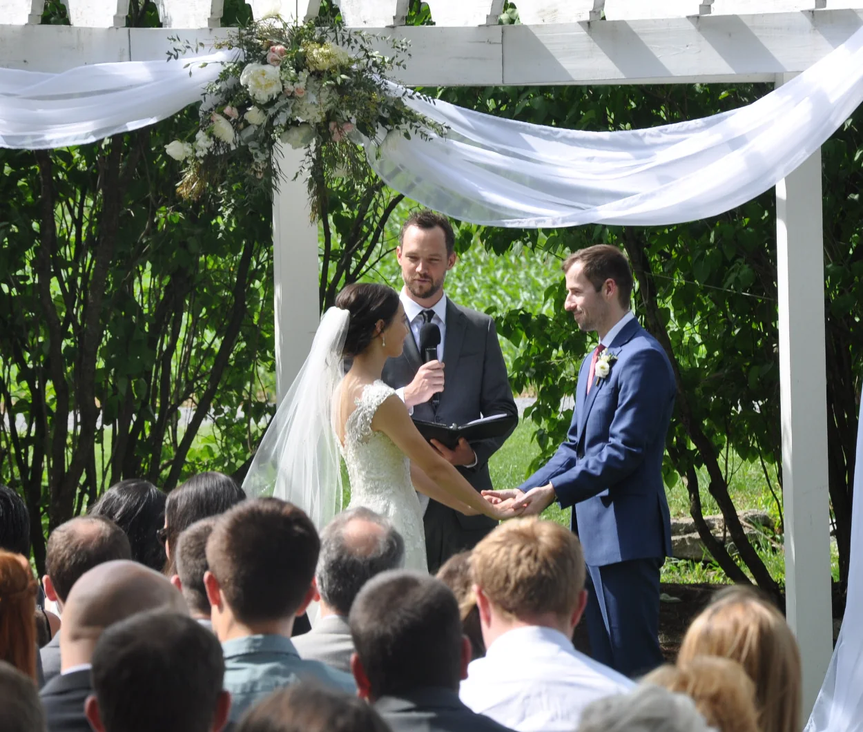Wedding officiant speaking during an outdoor ceremony while holding a handheld microphone away from the mouth