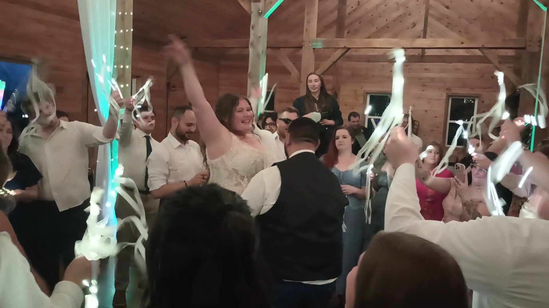 Bride celebrating on a packed wedding dance floor as guests wave glowing light sticks